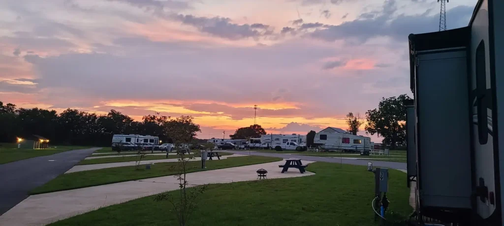 Sunset over an RV park with concrete pads, black picnic table, fire ring, hookup pedestal marked 39, and parked